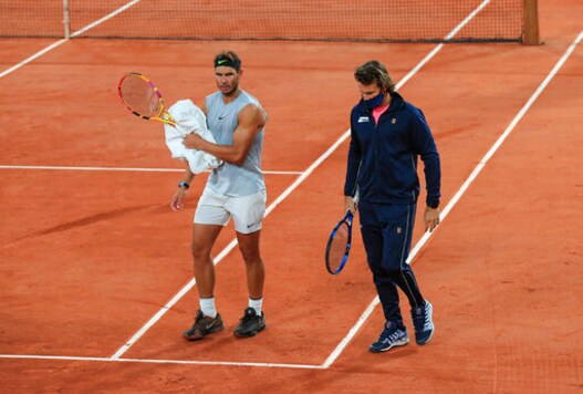 Spain's Rafael Nadal, left, and his coach Francisco Roig wearing a face mask to prevent the spread of coronavirus walk on the clay during practicing at the Roland Garros stadium in Paris, Friday, Sept. 25, 2020. Already repeatedly trimmed, crowd sizes for the French Open have been reduced again to just 1,000 spectators per day because of the worsening coronavirus epidemic in Paris. (AP Photo/Michel Euler)
