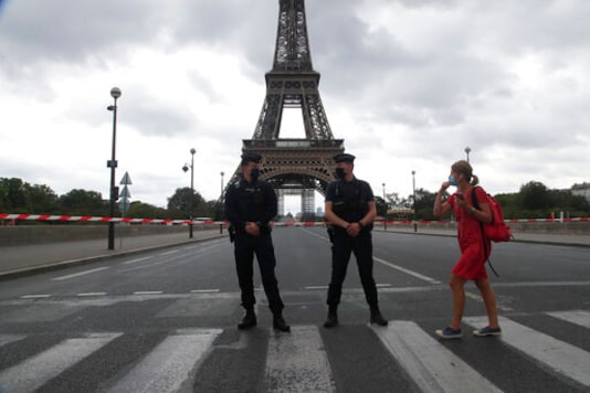 A woman walks past police officers securing the bridge leading to the Eiffel Tower, Wednesday, Sept. 23, 2020 in Paris. Paris police have blockaded the area around the Eiffel Tower after a phone-in bomb threat. (AP Photo/Michel Euler)