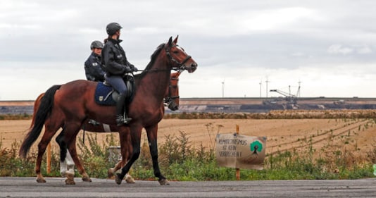 Police officers on horses secure the Garzweiler surface coal mine, passing a sign reading 'climate activism is not a crime' near Keyenberg, Germany, Friday, Sept. 25, 2020. Several groups like 'Friday for Future' or 'Ende Gelaende' started actions for climate justice in the coming days throughout Germany. The movement demands that the German government phase out coal by 2030 and make Germany carbon neutral by 2035. (AP Photo/Martin Meissner)