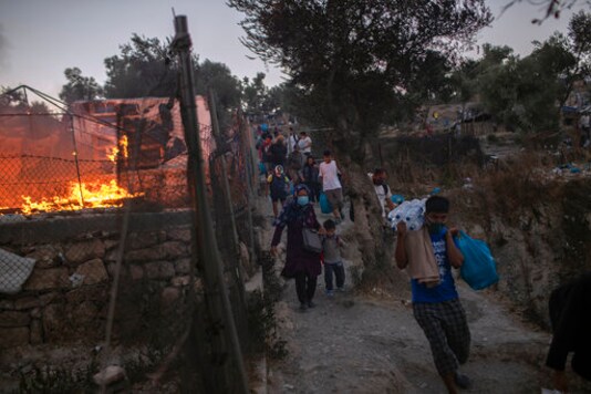 Refugees and migrants carrying their belongings flee a fire burning at the Moria camp on Lesbos island, Greece, Wednesday, Sept. 9, 2020. Fire struck for second day in Greece's notoriously overcrowded refugee camp, leaving more than 12,000 people in need of emergency shelter. (AP Photo/Petros Giannakouris)