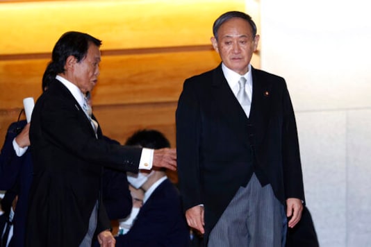 FILE - In this Sept. 16, 2020, file photo,  Japanese Prime Minister Yoshihide Suga, right, waits his cabinet members for a photo session after their first cabinet meeting at the prime minister's official residence in Tokyo. Prime Minister Suga's government says it will not look into scandals of a previous government, even though it is largely inheriting former leader's policies. (Yoshikazu Tsuno/Pool Photo via AP, File)