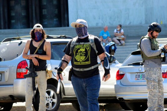 A protester wearing a t-shirt of a far-right group taunts Black Lives Matter protesters across the street in front of the Oregon State Capitol in Salem, Ore., on Monday, Sept. 7, 2020. Hundreds of people gathered on Labor Day in a small town south of Portland for a pro-President Donald Trump vehicle rally, just over a week after member of a far-right group was fatally shot after a Trump caravan went through Oregon's largest city. Later, pro-Trump supporters and counter-protesters clashed at Oregon's Capitol. (AP Photo/Andrew Selsky)