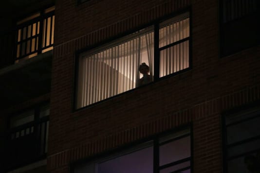 A woman looks out her window while protesters and police clash near the Mark O. Hatfield United States Courthouse on Saturday, Sept. 26, 2020, in Portland, Ore. (AP Photo/Allison Dinner)