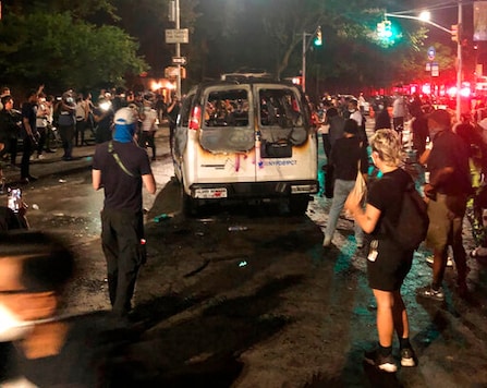 FILE - In this May 29, 2020 file photo, protesters stand near a burned New York City Police Department van in the Brooklyn borough of New York. Recent shootings of police officers and protests that have left scores of officers injured are stark reminders of the dangers facing law enforcement around a country grappling with police killings of African Americans. (AP Photo/Jim Mustian, File) FILE - In this May 29, 2020 file photo, protesters stand near a burned New York City Police Department van in the Brooklyn borough of New York. Recent shootings of police officers and protests that have left scores of officers injured are stark reminders of the dangers facing law enforcement around a country grappling with police killings of African Americans. (AP Photo/Jim Mustian, File)