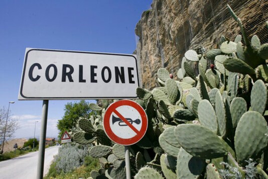 FILE -- In this file photo taken on April 12, 2006, a road sign announces the town of Corleone, Italy. The Sicilian town of Corleone, made famous by the fictional Mafia clan in The Godfather, has ordered schools closed and a limited lockdown after a spate of coronavirus infections were tied to a big wedding there last week. (AP Photo/Luca Bruno)