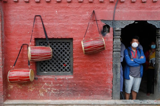 A Nepalese man waits for his turn to perform rituals as traditional drums are seen hanging on the wall during Gunla festival at Swayembhunath Stupa in Kathmandu, Nepal, Friday, Aug. 7, 2020. Autumn is the festival season in predominantly Hindu Nepal, where religion, celebrations and rituals are big parts of lives, but people this year will have to scale down their rituals within their homes. (AP Photo/Niranjan Shrestha)