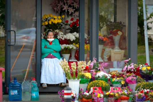 A flower vendor with a mask for protection against the COVID-19 infection, partially covering her face watches people passing by in Bucharest, Romania, Friday, Sept. 18, 2020. (AP Photo/Andreea Alexandru)