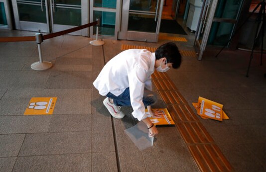 A man wearing a face mask attaches social distancing signs on the floor at the National Museum of Korea in Seoul, South Korea, Monday, Sept. 28, 2020. The museum reopened Monday after having been closed for six weeks as a precaution against the coronavirus. (AP Photo/Lee Jin-man)