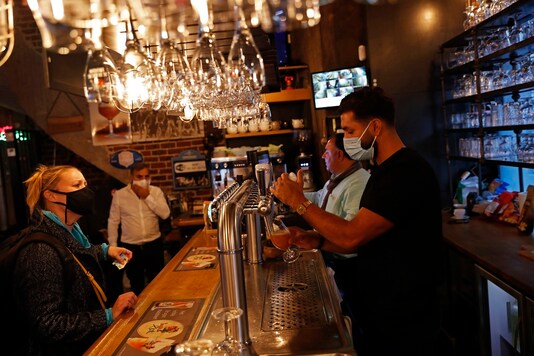 A bartender, wearing a face mask serves a beer to a customer in a pub in Brussels. (Credit: AP Photo)