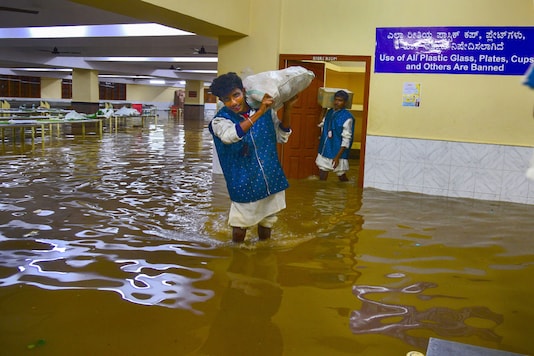 A worker carrying a sack wades through the waterlogged basement of a marriage hall in Bengaluru on Wednesday. (PTI) A worker carrying a sack wades through the waterlogged basement of a marriage hall in Bengaluru on Wednesday. (PTI)