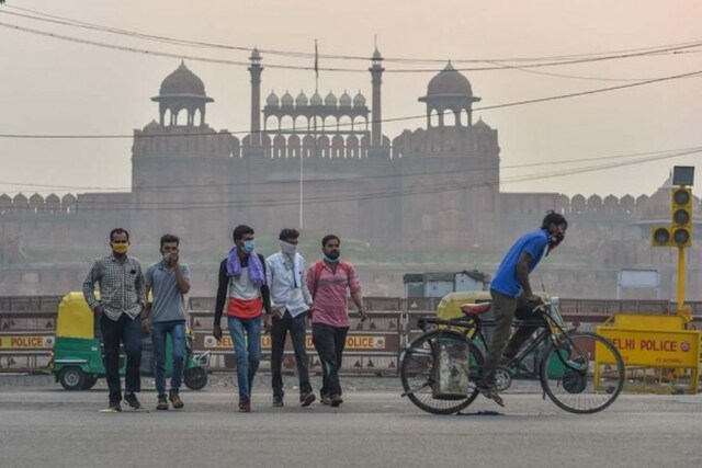 A man rides a cycle as commuters cross a road in front of the historic Red Fort during hazy weather conditions, in New Delhi. (Image: PTI)