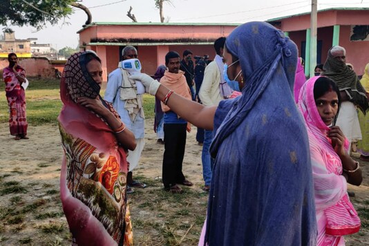 A volunteer checks temperature of voters at a polling station in Jamui.