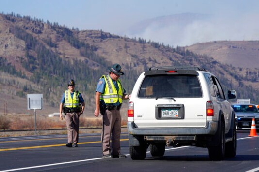 As smoke rises from mountain ridges, Colorado State Partrol troopers stop motorists at a roadblock on Highway 34 as a wildfire burns Thursday, Oct. 22, 2020, near Granby, Colo. (AP Photo/David Zalubowski)