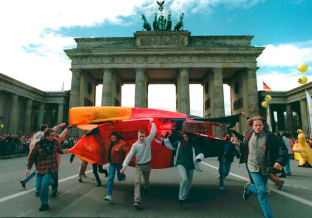 FILE - In this Sunday, Oct. 1, 1995 file photo, youth dance under a giant German flag in front of the Brandenburg Gate in Berlin  during a parade marking the fifth anniversary of German unification. Karsten Thielker, a Pulitzer Prize-winning German photographer with The Associated Press who covered human suffering in conflict zones around the globe, has died. He was 54. Thielker died Oct. 3 in Berlin of esophageal cancer, his wife Janna Ressel said Thursday, Oct. 8, 2020.(AP Photo/Karsten Thielker, file)
