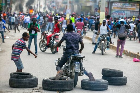 A motorcyclist uses his feet to drag tires into place for a barricade during a protest to demand the resignation of President Jovenel Moise in Port-au-Prince, Haiti, Saturday, Oct. 17, 2020. The country is currently experiencing a political impasse without a parliament and is now run entirely by decree under Moise. ( AP Photo/Dieu Nalio Chery) A motorcyclist uses his feet to drag tires into place for a barricade during a protest to demand the resignation of President Jovenel Moise in Port-au-Prince, Haiti, Saturday, Oct. 17, 2020. The country is currently experiencing a political impasse without a parliament and is now run entirely by decree under Moise. ( AP Photo/Dieu Nalio Chery)