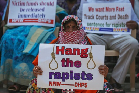 An activist with her face covered as a precautionary measure against the coronavirus holds a placard during a protest against the rape. (AP)