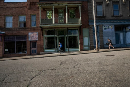 A boy rides his bicycle while a girl runs with her skateboard past abandoned storefronts along the streets of Shawnee, Ohio, on Friday, July 24, 2020. Shawnee was a coal town that once boasted an opera house, a vaudeville theater, dozens of stores and plenty of taverns. Today, Main Street is little but one abandoned building after another. (AP Photo/Wong Maye-E) A boy rides his bicycle while a girl runs with her skateboard past abandoned storefronts along the streets of Shawnee, Ohio, on Friday, July 24, 2020. Shawnee was a coal town that once boasted an opera house, a vaudeville theater, dozens of stores and plenty of taverns. Today, Main Street is little but one abandoned building after another. (AP Photo/Wong Maye-E)