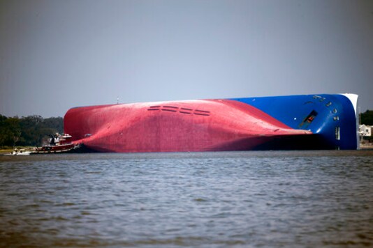 FILE - In this Sept. 9, 2019, file photo, a Moran tugboat nears the stern of the capsizing vessel Golden Ray near St. Simons Sound off the coast of Georgia. The salvage team is seeking a federal permit to surround the shipwreck with a giant mesh barrier to contain any debris when they cut the ship apart. Salvage workers coming to the Georgia coast to cut apart and remove the cargo ship that overturned will be isolated at a nearby resort to protect them from the coronavirus, officials said Tuesday, Sept. 8, 2020. (AP Photo/Stephen B. Morton, File) FILE - In this Sept. 9, 2019, file photo, a Moran tugboat nears the stern of the capsizing vessel Golden Ray near St. Simons Sound off the coast of Georgia. The salvage team is seeking a federal permit to surround the shipwreck with a giant mesh barrier to contain any debris when they cut the ship apart. Salvage workers coming to the Georgia coast to cut apart and remove the cargo ship that overturned will be isolated at a nearby resort to protect them from the coronavirus, officials said Tuesday, Sept. 8, 2020. (AP Photo/Stephen B. Morton, File)