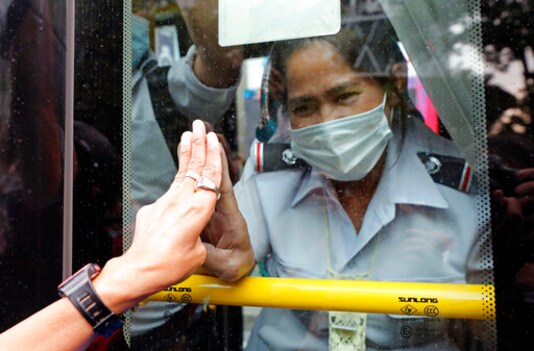 A pro-democracy protester, left, flashes three-fingered salutes to passengers on a bus in Bangkok, Thailand, Sunday, Oct. 25, 2020. Thailand's government and the country's pro-democracy movement appeared no closer to resolving their differences Saturday, as the protesters' deadline for Prime Minister Prayuth Chan-ocha to step down came and went with no new action from either side, and no backing down. (AP Photo/Sakchai Lalit)