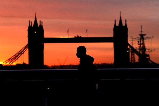 A person wearing a face mask to try to stop the spread of coronavirus walks across London Bridge, with Tower Bridge in the background, at sunrise in London, Monday, Oct. 12, 2020. In response to the coronavirus' resurgence, British Prime Minister Boris Johnson is expected to announce in Parliament on Monday a three-tier local lockdown system, formally known as A person wearing a face mask to try to stop the spread of coronavirus walks across London Bridge, with Tower Bridge in the background, at sunrise in London, Monday, Oct. 12, 2020. In response to the coronavirus' resurgence, British Prime Minister Boris Johnson is expected to announce in Parliament on Monday a three-tier local lockdown system, formally known as