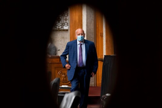 FILE - In this Wednesday, Sept. 16, 2020 file photo, Centers for Disease Control and Prevention Director Dr. Robert Redfield is seen through a door window as he appears at a Senate Appropriations subcommittee hearing on a FILE - In this Wednesday, Sept. 16, 2020 file photo, Centers for Disease Control and Prevention Director Dr. Robert Redfield is seen through a door window as he appears at a Senate Appropriations subcommittee hearing on a