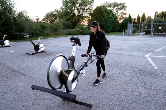 Jeanne Carter, co-owner of Fuel Training Studio, in Newburyport, Mass., removes stationary exercise bikes from a parking lot outside the gym following a spinning class, Monday, Sept. 21, 2020, in Newburyport. The gym's revenue is down about 60% during the COVID-19 pandemic. Fuel Training Studio plans to continue holding outdoor classes into the winter with the help of a planned greenhouse-like structure with heaters but no walls. (AP Photo/Steven Senne) Jeanne Carter, co-owner of Fuel Training Studio, in Newburyport, Mass., removes stationary exercise bikes from a parking lot outside the gym following a spinning class, Monday, Sept. 21, 2020, in Newburyport. The gym's revenue is down about 60% during the COVID-19 pandemic. Fuel Training Studio plans to continue holding outdoor classes into the winter with the help of a planned greenhouse-like structure with heaters but no walls. (AP Photo/Steven Senne)