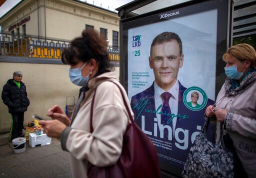 Women wearing face masks to protect against coronavirus wait at a bus stop, with a poster displaying Lithuania's Homeland Union Christian Democrats (TS-LKD) party member Mindaugas Linge, in Vilnius, Lithuania, Thursday, Oct. 8, 2020. Lithuanians are voting in the first round of a parliamentary election on Sunday. (AP Photo/Mindaugas Kulbis) Women wearing face masks to protect against coronavirus wait at a bus stop, with a poster displaying Lithuania's Homeland Union Christian Democrats (TS-LKD) party member Mindaugas Linge, in Vilnius, Lithuania, Thursday, Oct. 8, 2020. Lithuanians are voting in the first round of a parliamentary election on Sunday. (AP Photo/Mindaugas Kulbis)