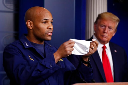 FILE - In this April 22, 2020 file photo President Donald Trump watches as U.S. Surgeon General Jerome Adams holds up his face mask as he speaks about the coronavirus in the James Brady Press Briefing Room of the White House, in Washington. Adams who was cited for being in a closed Hawaii park in August while in the islands helping with surge testing amid a spike in coronavirus cases, appears for a virtual arraignment in a Hawaii court on Wednesday, Oct. 21, 2020. (AP Photo/Alex Brandon,File) FILE - In this April 22, 2020 file photo President Donald Trump watches as U.S. Surgeon General Jerome Adams holds up his face mask as he speaks about the coronavirus in the James Brady Press Briefing Room of the White House, in Washington. Adams who was cited for being in a closed Hawaii park in August while in the islands helping with surge testing amid a spike in coronavirus cases, appears for a virtual arraignment in a Hawaii court on Wednesday, Oct. 21, 2020. (AP Photo/Alex Brandon,File)
