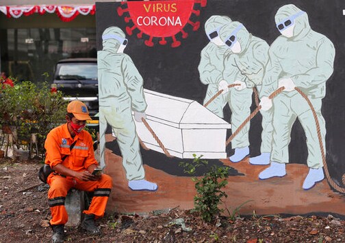 FILE - In this Aug. 14, 2020, file photo, a street sweeper checks his mobile phone as he takes a break near a coronavirus-themed mural in Jakarta, Indonesia. The World Bank has approved $12 billion in financing to help developing countries buy and distribute coronavirus vaccines, tests, and treatments, aiming to support the vaccination of up to 1 billion people, the bank said in a statement late Tuesday, Oct. 13, 2020. (AP Photo/Tatan Syuflana, File) FILE - In this Aug. 14, 2020, file photo, a street sweeper checks his mobile phone as he takes a break near a coronavirus-themed mural in Jakarta, Indonesia. The World Bank has approved $12 billion in financing to help developing countries buy and distribute coronavirus vaccines, tests, and treatments, aiming to support the vaccination of up to 1 billion people, the bank said in a statement late Tuesday, Oct. 13, 2020. (AP Photo/Tatan Syuflana, File)