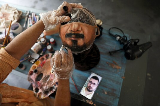 Plastic artist Jorge Silva Roriz paints a customized protective mask looking at man's photo on his cell phone, amid the outbreak of the coronavirus disease (COVID-19), at his home in Rio de Janeiro, Brazil November 10, 2020. Picture taken November 10, 2020. REUTERS/Pilar Olivares
