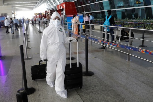 A person wearing personal protective equipment (PPE) carries luggage at an airport. (Reuters)