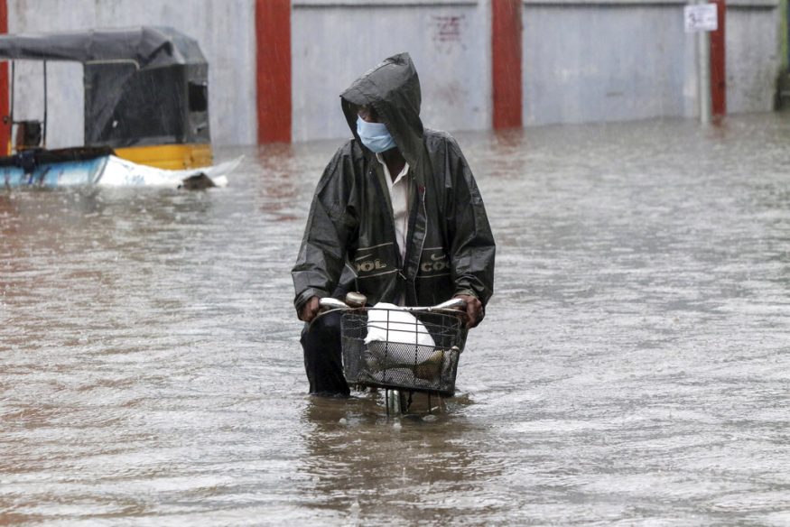  A man wearing a mask as a precaution against the coronavirus pedals his cycle through a flooded street in Chennai. (Image: AP)