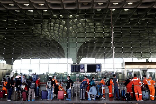 Passengers wearing protective face masks wait in a queue to enter Chhatrapati Shivaji International Airport. (REUTERS)