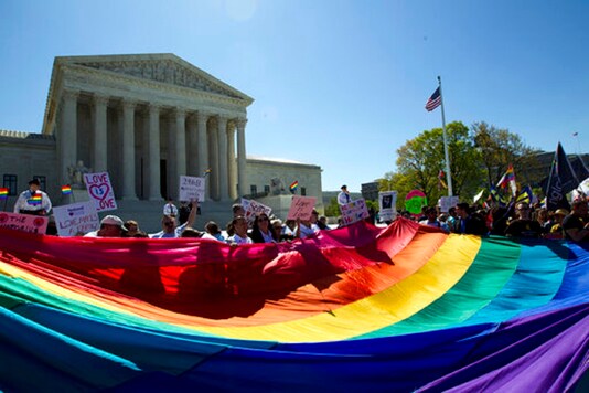 Demonstrators stand in front of a rainbow flag of the Supreme Court in Washington. 