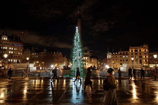 People wearing face masks walk past the illuminated Norwegian Christmas tree, after its lights were turned on without the usual ceremony to prevent people gathering in London's Trafalgar Square, Thursday, Dec 3, 2020. (Image: AP Photo/Matt Dunham)