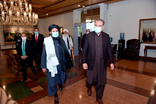In this photo provided by Pakistan's Ministry of Foreign Affairs, Pakistan's Foreign Minister Shah Mahmood Qureshi, right, and Mullah Abdul Ghani Baradar, head of a Taliban political team, arrive with other members of their delegations at the Foreign Ministry for talks, in Islamabad, Pakistan, Wednesday, Dec. 16, 2020. (Pakistan Ministry of Foreign Affairs via AP)