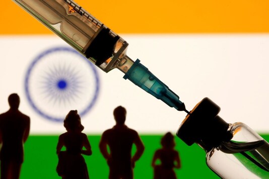 A vial, sryinge and small toy figures are seen in front of a displayed India flag in this illustration. (Image: Reuters)