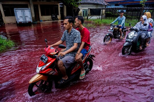 People ride motorbikes through a flooded road with red water due to the dye-waste from cloth factories, in Pekalongan, Central Java province, Indonesia.(Harviyan Perdana Putra/ via REUTERS)