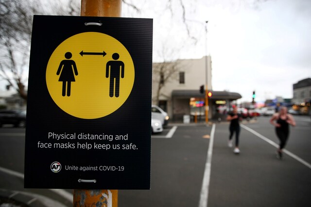 People jog past a social distancing sign on the first day of New Zealand's new coronavirus disease (COVID-19) safety measure that mandates wearing of a mask on public transport, in Auckland, New Zealand, August 31, 2020.  REUTERS/Fiona Goodall/File Photo
