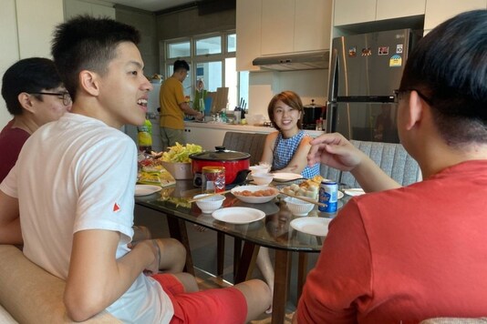 Chan Jit Yen smiles as she hosts Malaysian students, foreground, during a Lunar New Year hot pot lunch at her rented apartment in Singapore Saturday, Feb. 13, 2021. With Malaysian workers and students stranded in the city state over the Lunar New Year due to coronavirus travel restrictions, the Malaysian Association in Singapore has called on Malaysians to treat students to a meal. (AP Photo/Annabelle Liang).
