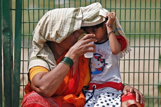 A woman offers water to her granddaughter as she covers her and herself to protect from sun stroke on a hot summer day in New Delhi. (Reuters)