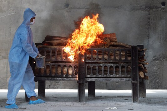 A frontline worker in PPE sprays a flammable liquid on a burning funeral pyre of a man who died from COVID-19 at a crematorium on the outskirts of Mumbai. (Reuters)