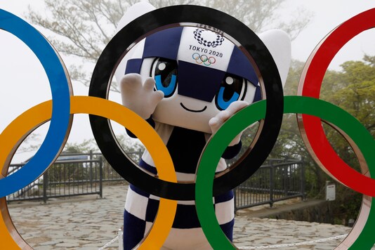 FILE - इस अप्रैल 14, 2021 में, फाइल फोटो, टोक्यो 2020 ओलंपिक खेलों के शुभंकर मिरिटोवा ने माउंट पर प्रतीक के अनावरण समारोह के बाद ओलंपिक प्रतीक का प्रदर्शन किया।  ओलंपिक खेलों की शुरुआत से 100 दिन पहले टोक्यो के पश्चिम में हाचियोजी में ताकाओ।  (एपी फोटो)