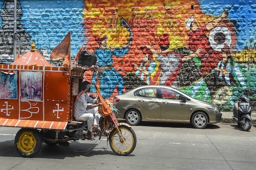 Workers drive past a wall mural in Mumbai, Sunday. (PTI)