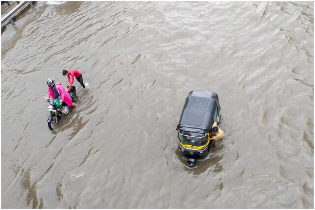 Commuters push their vehicles through a waterlogged street in Mumbai. (PTI Photo)