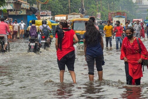 दिल्ली के जहांगीरपुरी इलाके में बारिश के बाद जलभराव वाली सड़क से गुजरते हुए यात्री।  (छवि: पीटीआई)