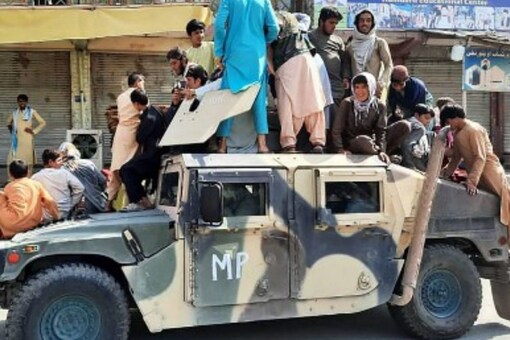 Taliban fighters and local residents sit over an Afghan National Army (ANA) humvee vehicle along the roadside in Laghman province on August 15, 2021. (AFP)