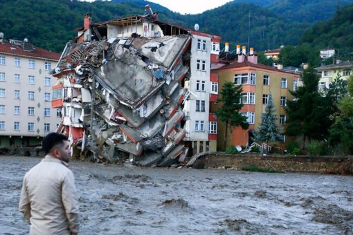 A man looks on as flood waters sweep by in Bozkurt town of Kastamonu province of Turkey, Thursday, Aug. 12, 2021. The floods triggered by torrential rains battered the Black Sea coastal provinces of Bartin, Kastamonu, Sinop and Samsun on Wednesday, demolishing homes and bridges and sweeping cars away by torrents. Helicopters scrambled to rescue people stranded on rooftops.(IHA via AP)