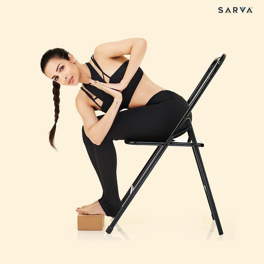 Malaika Arora does a namaste using two props - chair and brick. 
