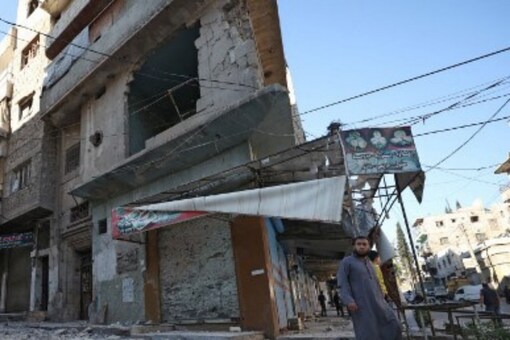 People walk past debris at the site of shelling in the Syrian town of Ariha in the rebel-held northwestern Syrian Idlib province on October 20, 2021. OMAR HAJ KADOUR / AFP